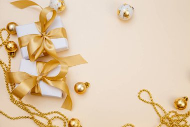 Beyaz hediyeler, altın fiyonklar ve bej arka planda ışıldayan süslemelerle süslü bir kış düzeni. Tebrik kartları, web pankartları ya da markalar için mükemmel.