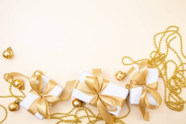 Beyaz hediyeler, altın fiyonklar ve bej arka planda ışıldayan süslemelerle süslü bir kış düzeni. Tebrik kartları, web pankartları ya da markalar için mükemmel.