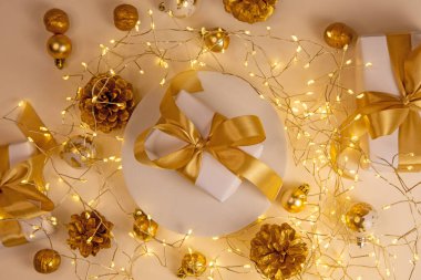 Parlayan çelenkleri, zarif hediyeleri, çam kozalakları ve süslemeleri olan altın bir Noel kompozisyonu. Mevsimsel selamlaşmalar ve şık markalaşma projeleri için kopya alanı olan rahat festival atmosferi.