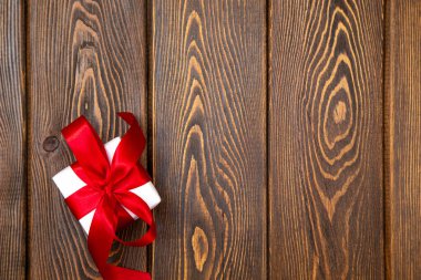 Ahşap arka planda kırmızı kurdeleli bir hediye kutusu. Bayram tebrik kartı ya da mevsimlik tasarım için kopya alanı olan en az festival kompozisyonu