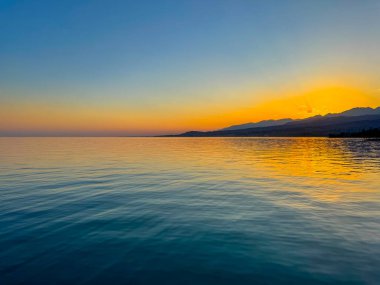 Kırgızistan 'daki Issyk Kul Gölü üzerinde gün batımı. Güneş dağların arkasında batar, suyun üzerinde altın bir yansıma bırakır. Kırgızistan 'daki Issyk Kul Gölü üzerinde gün batımında suyun üzerinde altın yansımasıyla.