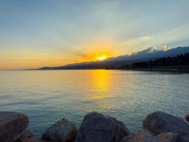 Kırgızistan 'daki Issyk Kul Gölü üzerinde gün batımı. Güneş dağların arkasında batar, suyun üzerinde altın bir yansıma bırakır. Kırgızistan 'daki Issyk Kul Gölü üzerinde gün batımında suyun üzerinde altın yansımasıyla.