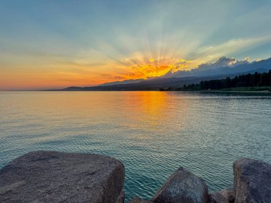 Kırgızistan 'daki Issyk Kul Gölü üzerinde gün batımı. Güneş dağların arkasında batar, suyun üzerinde altın bir yansıma bırakır. Kırgızistan 'daki Issyk Kul Gölü üzerinde gün batımında suyun üzerinde altın yansımasıyla.