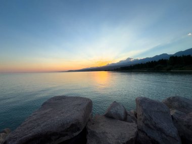 Kırgızistan 'daki Issyk Kul Gölü üzerinde gün batımı. Güneş dağların arkasında batar, suyun üzerinde altın bir yansıma bırakır. Kırgızistan 'daki Issyk Kul Gölü üzerinde gün batımında suyun üzerinde altın yansımasıyla.