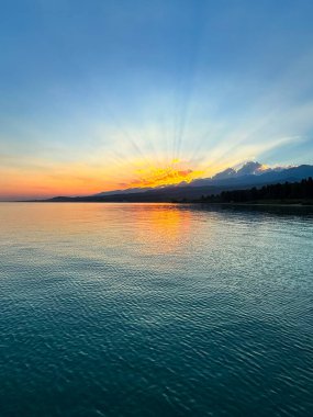 Kırgızistan 'daki Issyk Kul Gölü üzerinde gün batımı. Güneş dağların arkasında batar, suyun üzerinde altın bir yansıma bırakır. Kırgızistan 'daki Issyk Kul Gölü üzerinde gün batımında suyun üzerinde altın yansımasıyla.