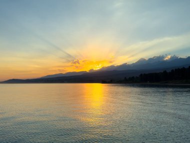 Kırgızistan 'daki Issyk Kul Gölü üzerinde gün batımı. Güneş dağların arkasında batar, suyun üzerinde altın bir yansıma bırakır. Kırgızistan 'daki Issyk Kul Gölü üzerinde gün batımında suyun üzerinde altın yansımasıyla.
