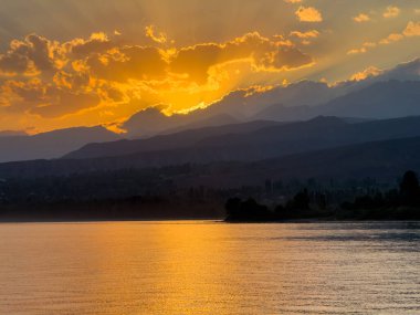 Kırgızistan 'daki Issyk Kul Gölü üzerinde gün batımı. Güneş dağların arkasında batar, suyun üzerinde altın bir yansıma bırakır. Kırgızistan 'daki Issyk Kul Gölü üzerinde gün batımında suyun üzerinde altın yansımasıyla.