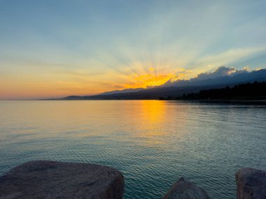 Kırgızistan 'daki Issyk Kul Gölü üzerinde gün batımı. Güneş dağların arkasında batar, suyun üzerinde altın bir yansıma bırakır. Kırgızistan 'daki Issyk Kul Gölü üzerinde gün batımında suyun üzerinde altın yansımasıyla.