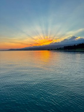 Kırgızistan 'daki Issyk Kul Gölü üzerinde gün batımı. Güneş dağların arkasında batar, suyun üzerinde altın bir yansıma bırakır. Kırgızistan 'daki Issyk Kul Gölü üzerinde gün batımında suyun üzerinde altın yansımasıyla.