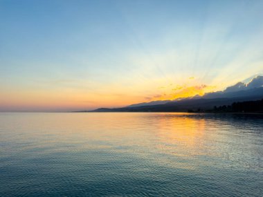 Kırgızistan 'daki Issyk Kul Gölü üzerinde gün batımı. Güneş dağların arkasında batar, suyun üzerinde altın bir yansıma bırakır. Kırgızistan 'daki Issyk Kul Gölü üzerinde gün batımında suyun üzerinde altın yansımasıyla.