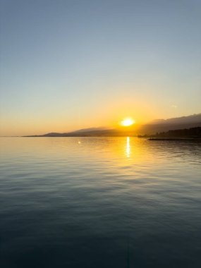 Kırgızistan 'daki Issyk Kul Gölü üzerinde gün batımı. Güneş dağların arkasında batar, suyun üzerinde altın bir yansıma bırakır. Kırgızistan 'daki Issyk Kul Gölü üzerinde gün batımında suyun üzerinde altın yansımasıyla.