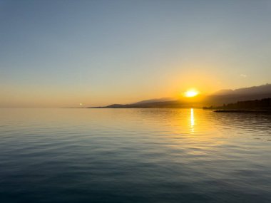Kırgızistan 'daki Issyk Kul Gölü üzerinde gün batımı. Güneş dağların arkasında batar, suyun üzerinde altın bir yansıma bırakır. Kırgızistan 'daki Issyk Kul Gölü üzerinde gün batımında suyun üzerinde altın yansımasıyla.
