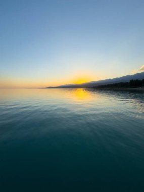 Kırgızistan 'daki Issyk Kul Gölü üzerinde gün batımı. Güneş dağların arkasında batar, suyun üzerinde altın bir yansıma bırakır. Kırgızistan 'daki Issyk Kul Gölü üzerinde gün batımında suyun üzerinde altın yansımasıyla.