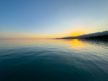 Kırgızistan 'daki Issyk Kul Gölü üzerinde gün batımı. Güneş dağların arkasında batar, suyun üzerinde altın bir yansıma bırakır. Kırgızistan 'daki Issyk Kul Gölü üzerinde gün batımında suyun üzerinde altın yansımasıyla.