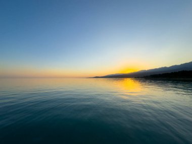 Kırgızistan 'daki Issyk Kul Gölü üzerinde gün batımı. Güneş dağların arkasında batar, suyun üzerinde altın bir yansıma bırakır. Kırgızistan 'daki Issyk Kul Gölü üzerinde gün batımında suyun üzerinde altın yansımasıyla.