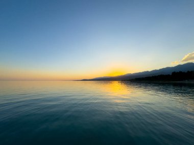 Kırgızistan 'daki Issyk Kul Gölü üzerinde gün batımı. Güneş dağların arkasında batar, suyun üzerinde altın bir yansıma bırakır. Kırgızistan 'daki Issyk Kul Gölü üzerinde gün batımında suyun üzerinde altın yansımasıyla.