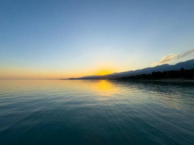 Kırgızistan 'daki Issyk Kul Gölü üzerinde gün batımı. Güneş dağların arkasında batar, suyun üzerinde altın bir yansıma bırakır. Kırgızistan 'daki Issyk Kul Gölü üzerinde gün batımında suyun üzerinde altın yansımasıyla.