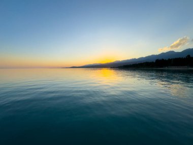 Kırgızistan 'daki Issyk Kul Gölü üzerinde gün batımı. Güneş dağların arkasında batar, suyun üzerinde altın bir yansıma bırakır. Kırgızistan 'daki Issyk Kul Gölü üzerinde gün batımında suyun üzerinde altın yansımasıyla.