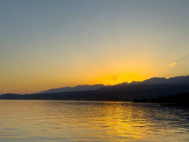 Kırgızistan 'daki Issyk Kul Gölü üzerinde gün batımı. Güneş dağların arkasında batar, suyun üzerinde altın bir yansıma bırakır. Kırgızistan 'daki Issyk Kul Gölü üzerinde gün batımında suyun üzerinde altın yansımasıyla.