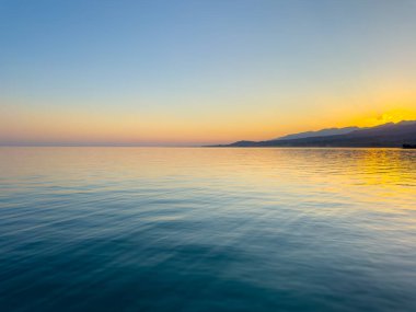 Kırgızistan 'daki Issyk Kul Gölü üzerinde gün batımı. Güneş dağların arkasında batar, suyun üzerinde altın bir yansıma bırakır. Kırgızistan 'daki Issyk Kul Gölü üzerinde gün batımında suyun üzerinde altın yansımasıyla.