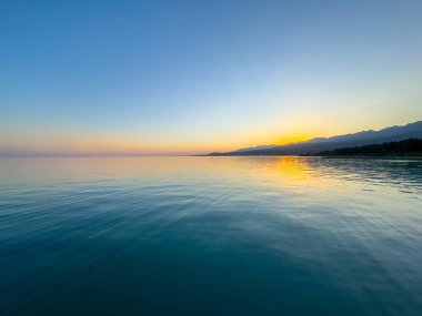 Kırgızistan 'daki Issyk Kul Gölü üzerinde gün batımı. Güneş dağların arkasında batar, suyun üzerinde altın bir yansıma bırakır. Kırgızistan 'daki Issyk Kul Gölü üzerinde gün batımında suyun üzerinde altın yansımasıyla.