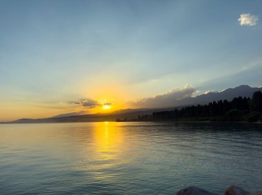 Kırgızistan 'daki Issyk Kul Gölü üzerinde gün batımı. Güneş dağların arkasında batar, suyun üzerinde altın bir yansıma bırakır. Kırgızistan 'daki Issyk Kul Gölü üzerinde gün batımında suyun üzerinde altın yansımasıyla.