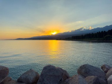 Kırgızistan 'daki Issyk Kul Gölü üzerinde gün batımı. Güneş dağların arkasında batar, suyun üzerinde altın bir yansıma bırakır. Kırgızistan 'daki Issyk Kul Gölü üzerinde gün batımında suyun üzerinde altın yansımasıyla.