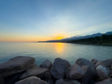 Kırgızistan 'daki Issyk Kul Gölü üzerinde gün batımı. Güneş dağların arkasında batar, suyun üzerinde altın bir yansıma bırakır. Kırgızistan 'daki Issyk Kul Gölü üzerinde gün batımında suyun üzerinde altın yansımasıyla.