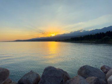 Kırgızistan 'daki Issyk Kul Gölü üzerinde gün batımı. Güneş dağların arkasında batar, suyun üzerinde altın bir yansıma bırakır. Kırgızistan 'daki Issyk Kul Gölü üzerinde gün batımında suyun üzerinde altın yansımasıyla.