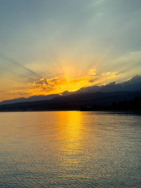 Kırgızistan 'daki Issyk Kul Gölü üzerinde gün batımı. Güneş dağların arkasında batar, suyun üzerinde altın bir yansıma bırakır. Kırgızistan 'daki Issyk Kul Gölü üzerinde gün batımında suyun üzerinde altın yansımasıyla.