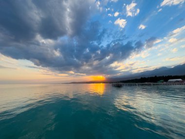 Kırgızistan 'daki Issyk Kul Gölü üzerinde gün batımı. Güneş dağların arkasında batar, suyun üzerinde altın bir yansıma bırakır. Kırgızistan 'daki Issyk Kul Gölü üzerinde gün batımında suyun üzerinde altın yansımasıyla.