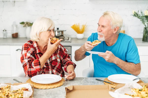 Senior couple eating pizza in the kitchen