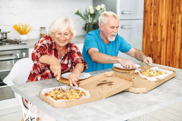 Senior couple eating pizza in the kitchen