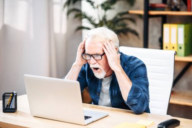 Yaşlı adam içeride çalışmak için dizüstü bilgisayar kullanıyor.