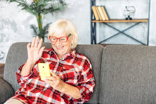 Starší žena sedí na pohovce s chytrým telefonem — Stock fotografie