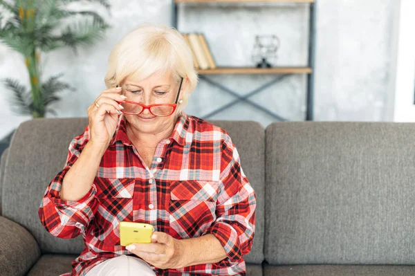 Старша жінка сидить на дивані зі смартфоном — стокове фото