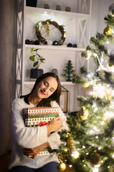 Μια νεαρή γυναίκα με ένα κουτί δώρου κοντά στο χριστουγεννιάτικο δέντρο. — Φωτογραφία Αρχείου