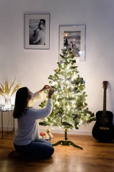 Eine Frau hängt Weihnachtskugeln an den Baum — Stockfoto