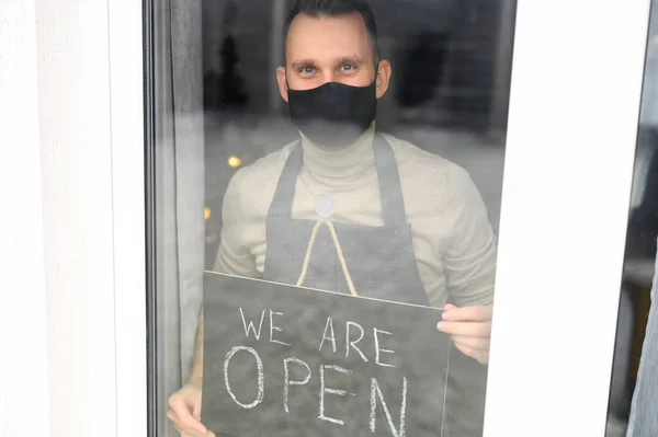 Jeune homme masqué tenant un panneau ouvert dans un café — Photo