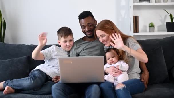 Una familia multirracial feliz de cuatro con un ordenador portátil — Vídeos de Stock