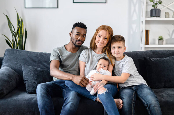 A multiracial family sits on the couch at home