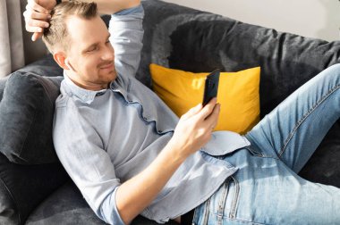 Kanepede akıllı telefonu olan bir adam.