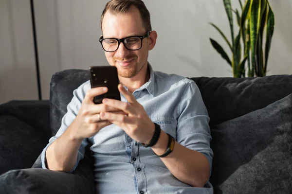 Un tipo con un teléfono inteligente se sienta en el sofá — Foto de Stock