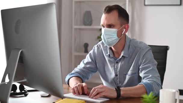 Парень в маске, использующий компьютер в офисе — стоковое видео
