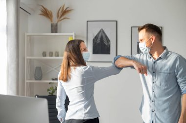 Alternatif bir tokalaşma sırasında ofiste selamlar. Tıbbi yüz maskesi takmış ofis çalışanları birbirlerine dirsek tokuşturup gülümsüyorlar. Koruyucu tedbirler
