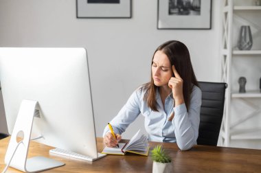 Odaklanmış mavi gömlekli genç bir kadın ofiste bir bilgisayarla çalışıyor, web sitesi izleyen bir iş kadını, video kursları ve notlar alıyor. Masada kalemle yazan bir girişimci kadın.