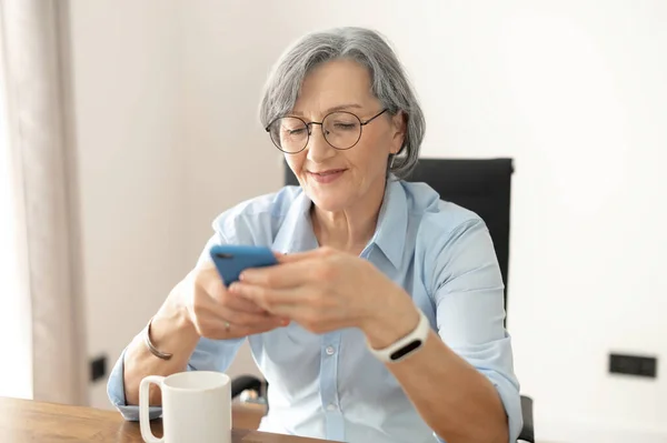 Starší žena pracuje na mobilním telefonu — Stock fotografie