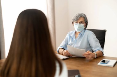 Yüz maskeli üst düzey kadın İK müdürü CV okuyor.