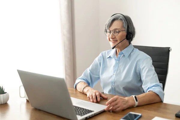 Elder woman sitting at the desk in a headset