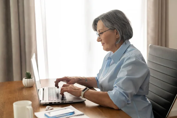 Femme d'affaires senior tapant sur un ordinateur portable de la maison — Photo